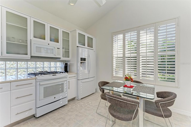 kitchen with lofted ceiling, white cabinetry, white appliances, and light tile patterned floors