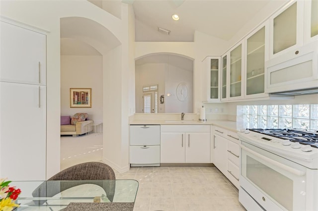 kitchen with lofted ceiling, white appliances, white cabinets, sink, and light tile patterned floors