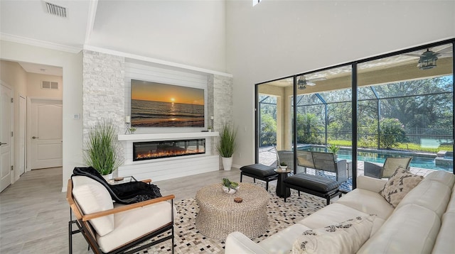 living room featuring a fireplace, a towering ceiling, light hardwood / wood-style flooring, and ornamental molding