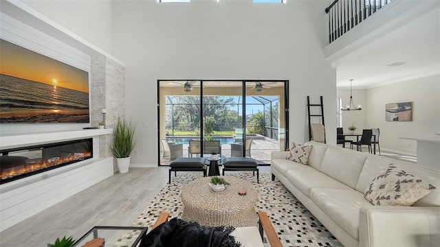 living room featuring light wood-type flooring, a large fireplace, crown molding, a notable chandelier, and a high ceiling