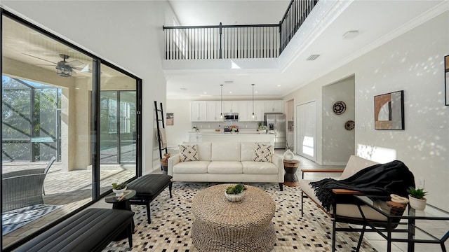 living room with a high ceiling, light wood-type flooring, ceiling fan, and crown molding