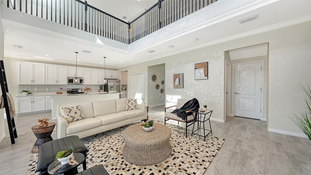 living room featuring light hardwood / wood-style flooring, a high ceiling, and ornamental molding