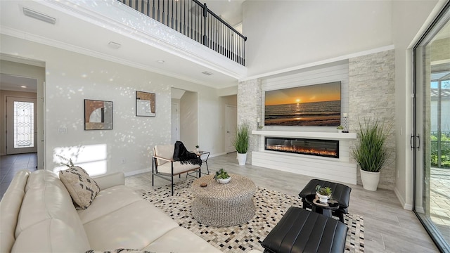 living room with ornamental molding, a fireplace, a high ceiling, and light hardwood / wood-style flooring