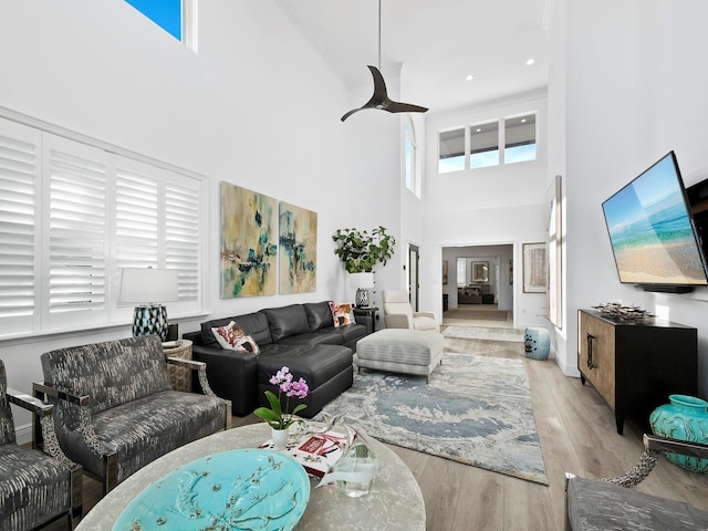 living room with a wealth of natural light, light hardwood / wood-style flooring, a towering ceiling, and ceiling fan