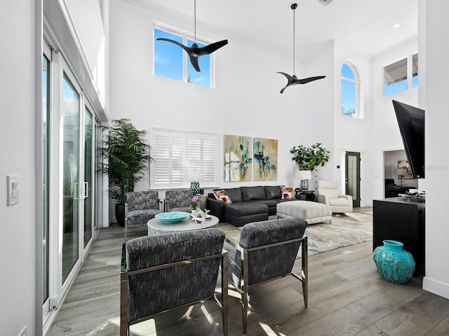 living room with ceiling fan, plenty of natural light, a towering ceiling, and wood-type flooring