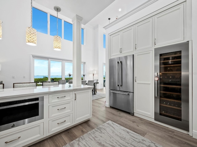 kitchen featuring appliances with stainless steel finishes, pendant lighting, light hardwood / wood-style flooring, white cabinets, and wine cooler