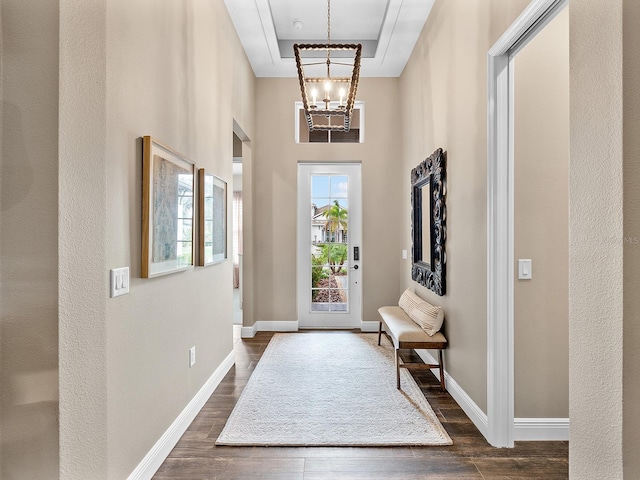 entrance foyer with a raised ceiling, an inviting chandelier, and dark wood-type flooring