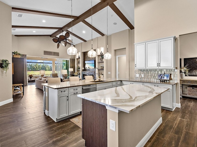 kitchen with beam ceiling, sink, light stone counters, a center island with sink, and white cabinets