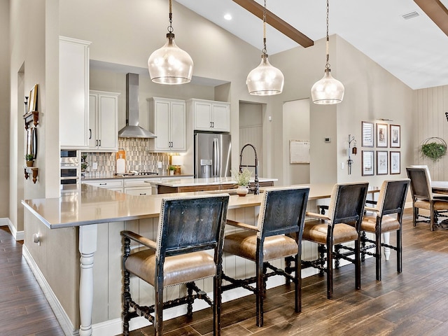 kitchen featuring pendant lighting, backsplash, white cabinets, wall chimney range hood, and stainless steel appliances