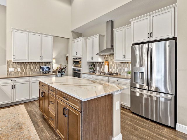 kitchen featuring white cabinets, wall chimney range hood, light stone countertops, appliances with stainless steel finishes, and a kitchen island