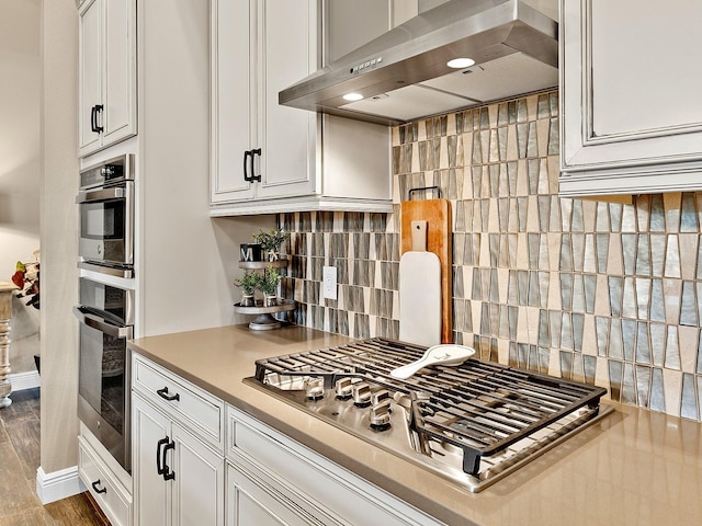 kitchen with tasteful backsplash, stainless steel gas cooktop, exhaust hood, light hardwood / wood-style flooring, and white cabinets