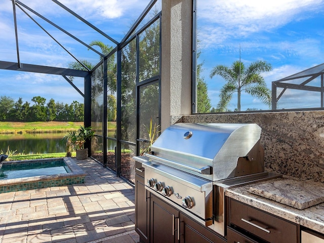 view of patio with an outdoor kitchen, a lanai, grilling area, an in ground hot tub, and a water view