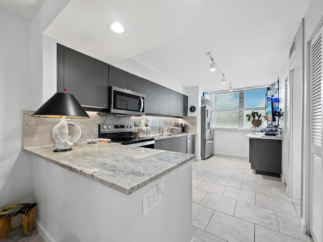 kitchen featuring kitchen peninsula, appliances with stainless steel finishes, backsplash, track lighting, and light stone countertops