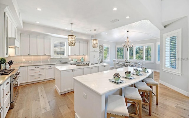 kitchen with a center island with sink, sink, hanging light fixtures, high end stove, and tasteful backsplash