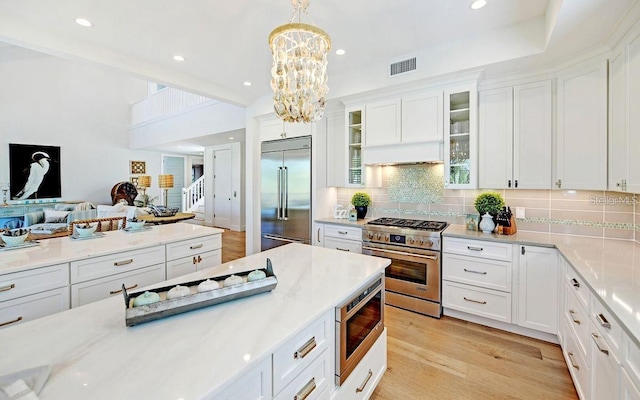 kitchen featuring light wood-type flooring, built in appliances, decorative light fixtures, and white cabinetry