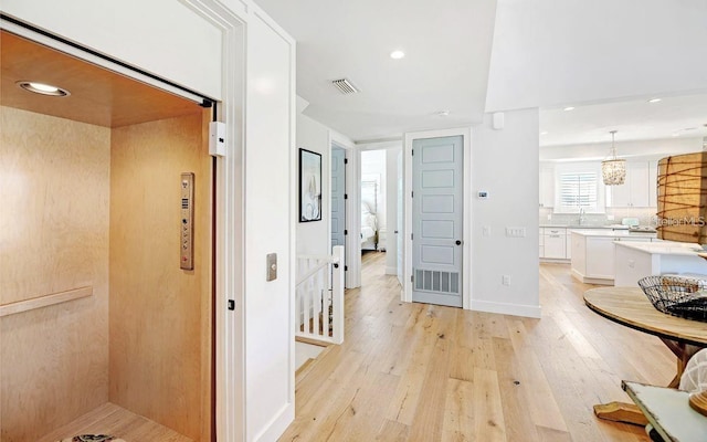 corridor featuring elevator, sink, and light wood-type flooring