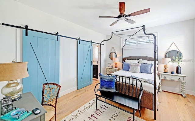 bedroom with a barn door, ceiling fan, ensuite bath, and light wood-type flooring