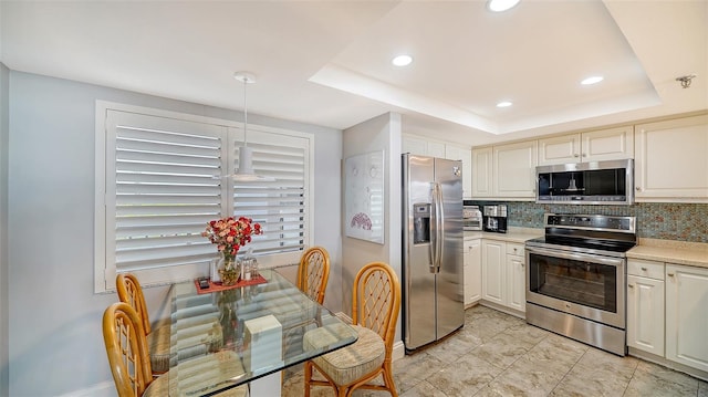 kitchen featuring pendant lighting, a raised ceiling, appliances with stainless steel finishes, and tasteful backsplash