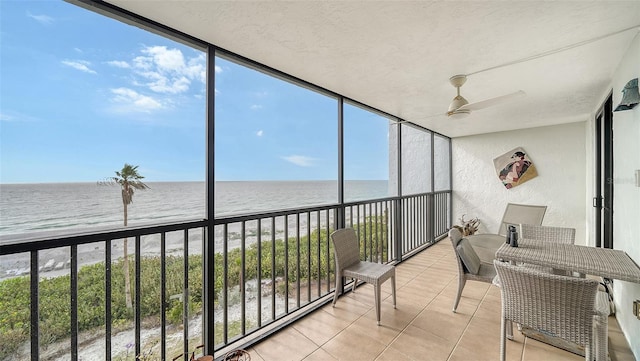 sunroom / solarium featuring ceiling fan, a water view, and a view of the beach