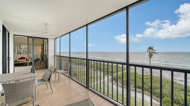 sunroom / solarium featuring ceiling fan, a water view, and a view of the beach