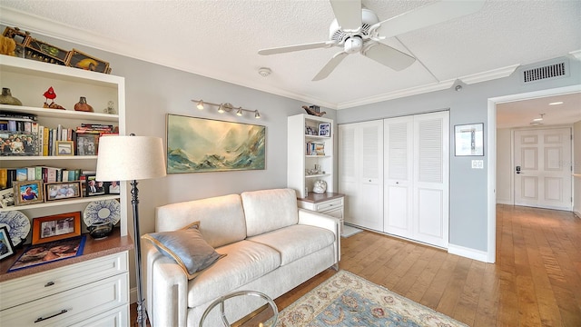 living room featuring crown molding, light hardwood / wood-style flooring, ceiling fan, and a textured ceiling