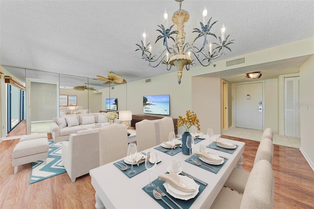 dining space with ceiling fan with notable chandelier, a textured ceiling, and light hardwood / wood-style flooring