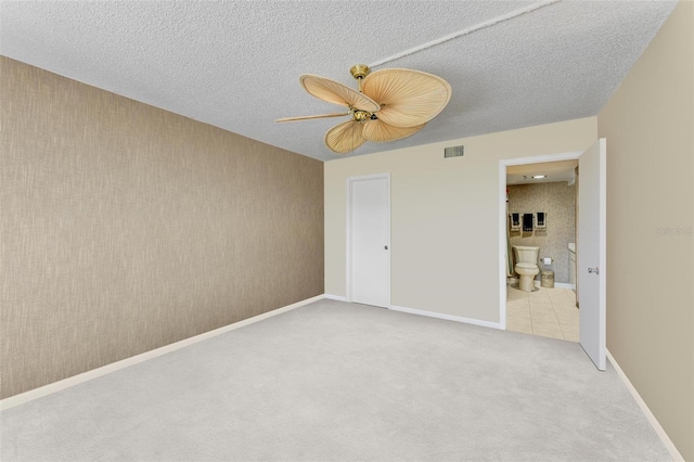 unfurnished bedroom featuring light carpet, a textured ceiling, connected bathroom, and ceiling fan