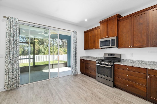 kitchen with light stone countertops, ceiling fan, light hardwood / wood-style floors, and appliances with stainless steel finishes