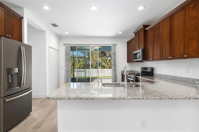 kitchen featuring light stone countertops, sink, light hardwood / wood-style flooring, kitchen peninsula, and appliances with stainless steel finishes