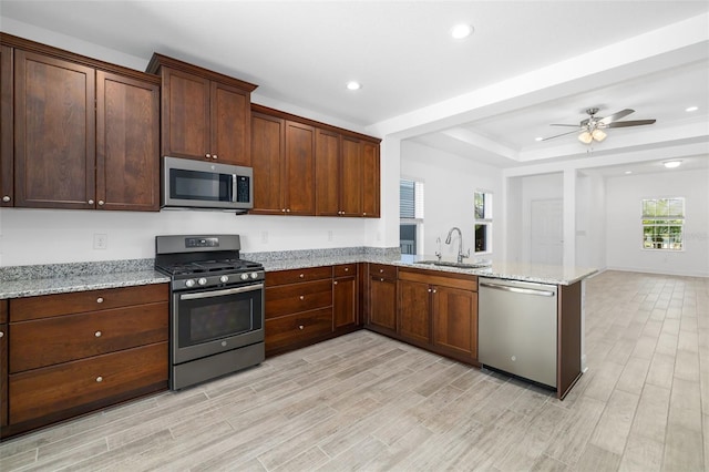 kitchen with light stone countertops, sink, kitchen peninsula, light hardwood / wood-style floors, and appliances with stainless steel finishes