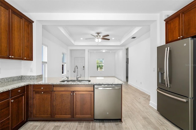 kitchen with light stone countertops, light wood-type flooring, stainless steel appliances, a raised ceiling, and sink