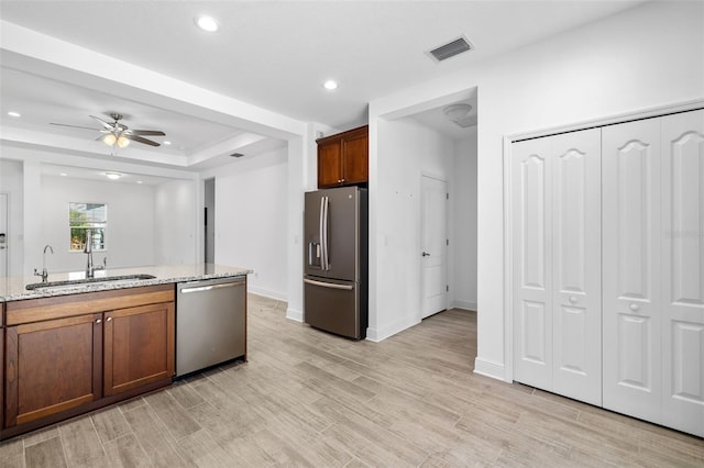 kitchen featuring ceiling fan, sink, light stone counters, light hardwood / wood-style floors, and appliances with stainless steel finishes