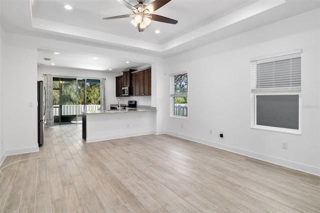 kitchen with kitchen peninsula, dark brown cabinets, light hardwood / wood-style floors, and a tray ceiling