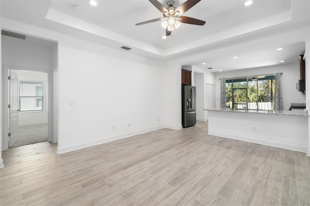 unfurnished living room with a raised ceiling, ceiling fan, and light hardwood / wood-style flooring