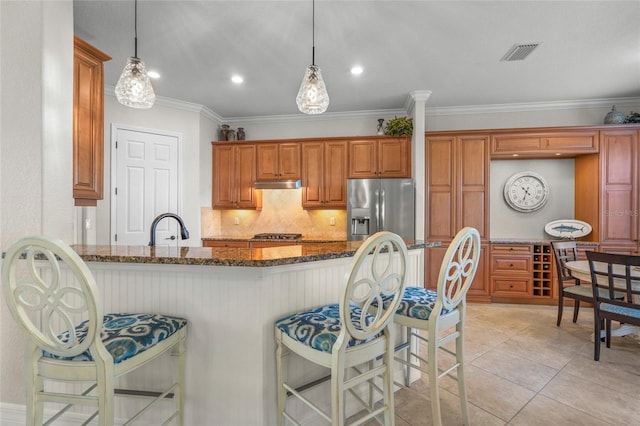 kitchen with appliances with stainless steel finishes, a kitchen breakfast bar, hanging light fixtures, and dark stone counters