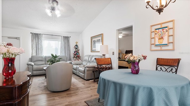 dining room with ceiling fan with notable chandelier, light hardwood / wood-style floors, and vaulted ceiling