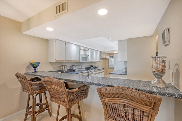 kitchen with stainless steel electric range, a kitchen bar, white cabinetry, and kitchen peninsula