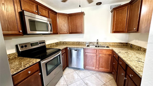 kitchen with light stone countertops, sink, light tile patterned floors, and appliances with stainless steel finishes