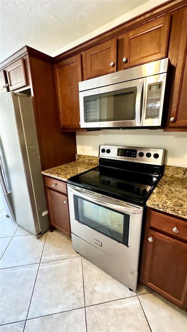 kitchen with light tile patterned floors, stainless steel appliances, and light stone counters