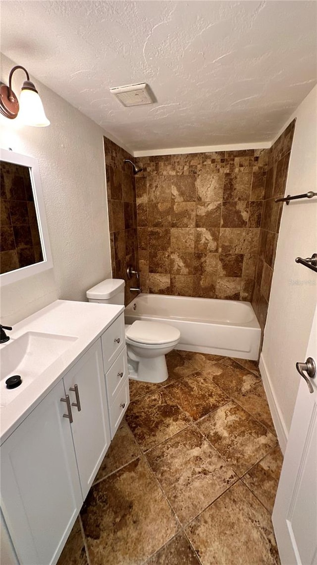 full bathroom with tiled shower / bath, vanity, a textured ceiling, and toilet