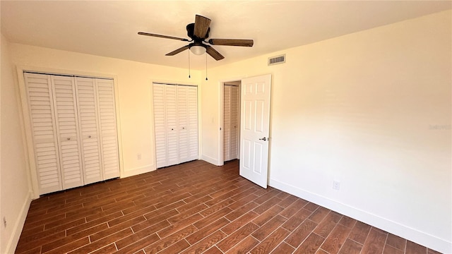 unfurnished bedroom with dark hardwood / wood-style flooring, two closets, and ceiling fan