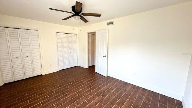 unfurnished bedroom with ceiling fan, dark hardwood / wood-style flooring, and multiple closets