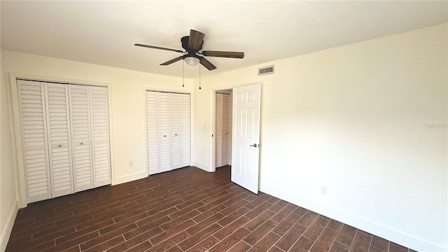 unfurnished bedroom featuring two closets, ceiling fan, and dark hardwood / wood-style floors