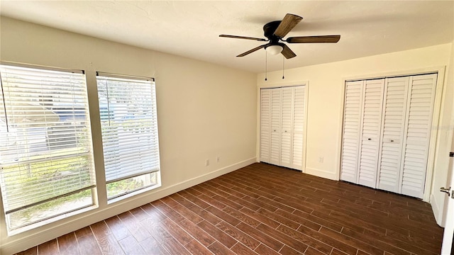 unfurnished bedroom featuring dark hardwood / wood-style floors, ceiling fan, and multiple closets