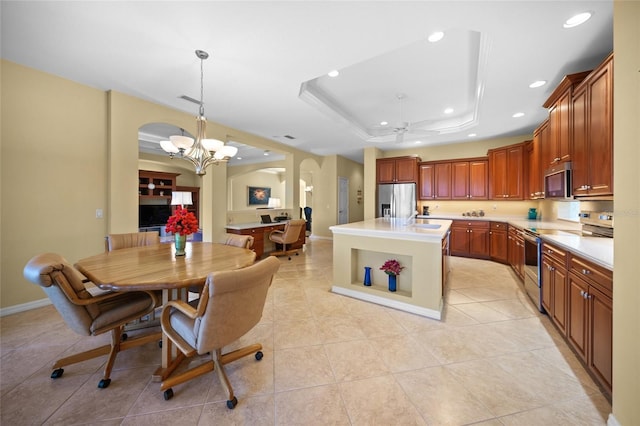 kitchen featuring pendant lighting, appliances with stainless steel finishes, a center island, ceiling fan with notable chandelier, and a raised ceiling