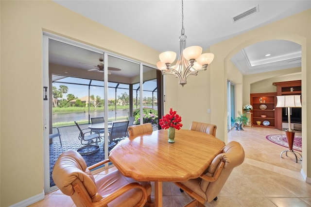 tiled dining room with a tray ceiling, ceiling fan with notable chandelier, crown molding, and a water view