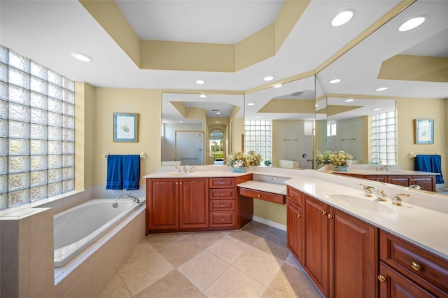 bathroom featuring a raised ceiling, vanity, a relaxing tiled tub, and tile patterned floors