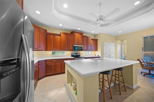 kitchen with a raised ceiling, sink, a breakfast bar area, a kitchen island with sink, and stainless steel appliances