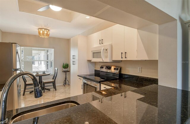 kitchen featuring appliances with stainless steel finishes, dark stone counters, sink, white cabinets, and light tile patterned flooring