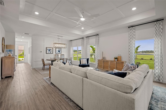 living room with ceiling fan with notable chandelier, coffered ceiling, and light wood-type flooring